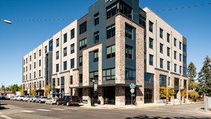 Un edificio moderno con un llamativo letrero de 'Regus', que presenta una fachada de ladrillo y vidrio, varios pisos y un estacionamiento al frente.