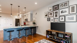 Una cocina moderna con una isla central, taburetes de bar, un televisor de pantalla plana y una estantería.