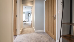 A hallway with a carpeted floor, wooden doors, and a shelf unit. - Tipyn O Haul - 1 Bed Apartment - Tenby (Tenby)