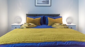 A neatly made bed with a blue and yellow bedspread, two pillows, and a yellow blanket. There is a framed picture on the wall above the bed. - Tipyn O Haul - 1 Bed Apartment - Tenby (Tenby)