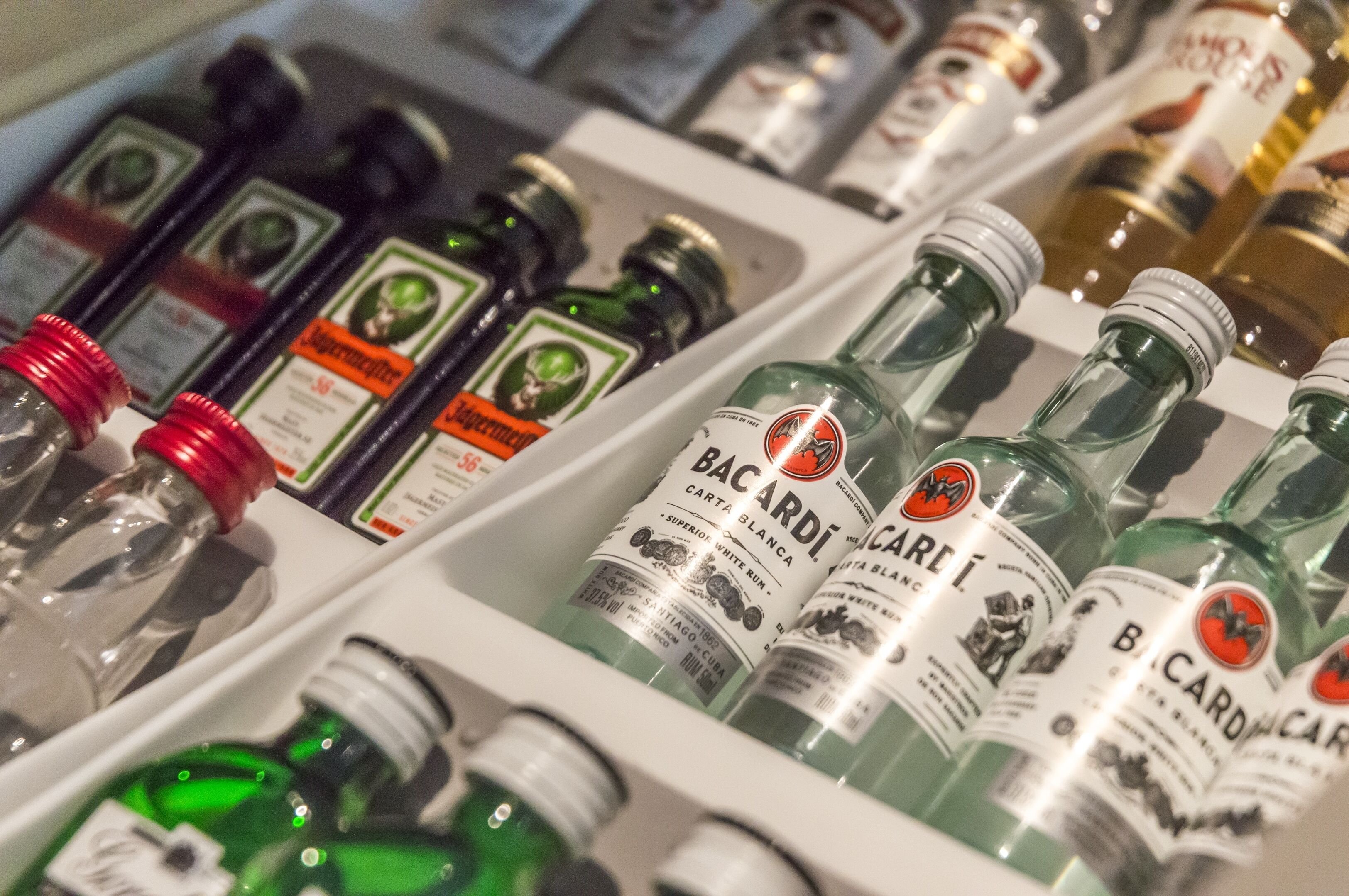 A refrigerated display of various liquor bottles, including Bacardi and Supermercado brands.