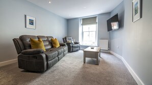 A modern living room with a grey leather sofa, a recliner, and a coffee table. - Tipyn O Haul - 1 Bed Apartment - Tenby (Tenby)