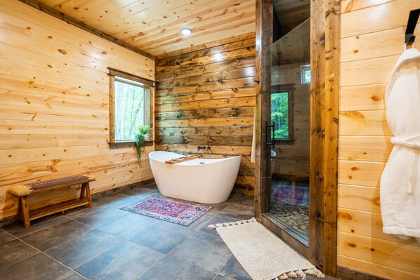 Baño de una cabaña de madera con una bañera independiente, un banco y una zona de ducha.