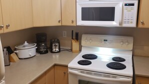 Una cocina con microondas blanco, estufa, tostadora y olla de cocción lenta.
