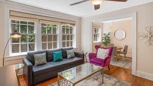 A living room with a dark gray sofa, a glass coffee table, a purple armchair, and a ceiling fan. - Oasis Overlooking Forsyth Park w/ Private Balcony & Parking by Lucky Savannah (Savannah)
