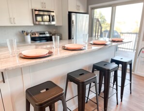 A modern kitchen with a marble countertop, stainless steel appliances, and bar stools. - Coastal Soul - Beach block, on cul-de-sac street, pet friendly. (Brigantine)
