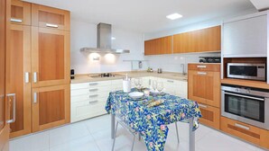 Une cuisine moderne avec des meubles en bois, un îlot central recouvert d’une nappe à motifs floraux et des appareils électroménagers intégrés.