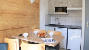 A compact kitchen with a microwave, sink, and white cabinets. A wooden dining table with chairs is set up in front. - 20m from ski slopes, 2nd floor, balcony, tv, ski locker, 25m², Serre Chevalier (Briançon)