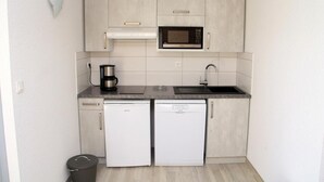 Uma cozinha compacta equipada com micro-ondas, cafeteira, pia e dois pequenos frigoríficos.