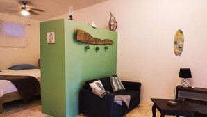 A room with a green accent wall, a black sofa with patterned cushions, a wooden coffee table, a ceiling fan, and a wall-mounted light fixture.