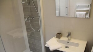 Ein modernes Badezimmer mit Duschkabine aus Glas, einem weißen Waschbecken mit Handtuch und einem Spiegel darüber.