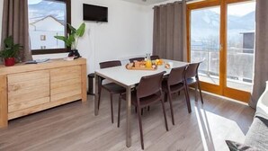 Un comedor con una mesa dispuesta para cuatro, un aparador de madera y un televisor montado en la pared.