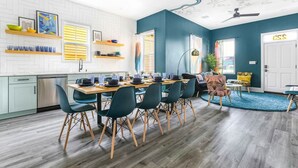 Una cocina moderna con azulejos blancos tipo metro, un comedor con mesa de madera y sillas verdes, y una sala de estar con un muro azul decorativo y un diseño de mapa en el techo.