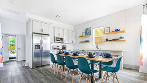 Una cocina moderna con armarios blancos, un refrigerador de acero inoxidable y un comedor con sillas color turquesa y una mesa de madera.