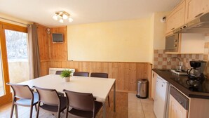 A compact kitchen with wooden cabinets, a dining table with chairs, a small trash bin, and a coffee maker. - 50m from ski slopes, 3rd floor, balcony, tv, ski locker, 38m², Serre Chevalier (Briançon)