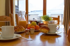 Aamiaispöydällä on croissantteja, kahvikuppi, hedelmäkulho ja kannullinen mehua.