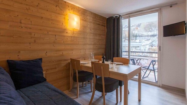 Une pièce chaleureuse avec un mur en bois, une table à manger avec des chaises, un canapé et un téléviseur fixé au mur.