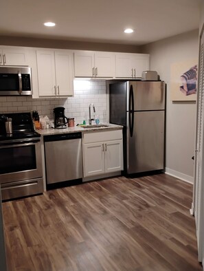 A compact kitchen with stainless steel appliances, white cabinets, and a wooden floor. - Walk to Nightlife & Attractions (Indianapolis)