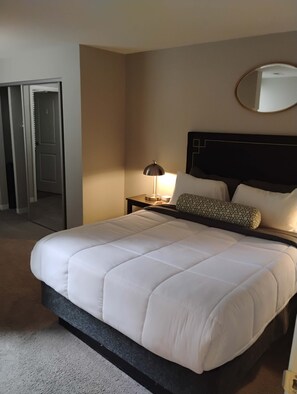 A hotel room with a large bed, a bedside table with a lamp, a mirror on the wall, and a door leading to another room. - Walk to Nightlife & Attractions (Indianapolis)