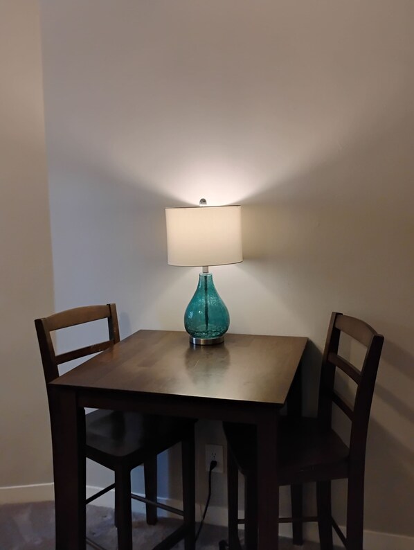 A dining table with two chairs, a teal glass lamp, and a power cord plugged into the wall.