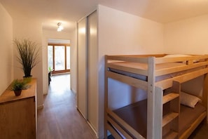 Compact room with bunk bed arrangement, desk area, and sliding door to adjacent living space.