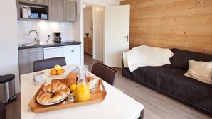 A modern kitchen with a dining area, a wooden wall, and a dark-colored sofa. - 50m from ski slopes, 2nd floor, balcony, tv, ski locker, 30m², Serre Chevalier (Briançon)