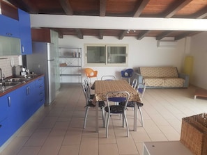 A compact kitchen with blue cabinets, a dining table with four chairs, and a sofa in the living area.