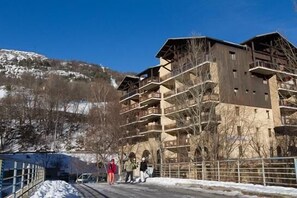 Ein mehrstöckiges Gebäude mit Balkonen, verschneitem Untergrund und blauem Himmel.