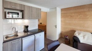 Une cuisine compacte équipée d’un four à micro-ondes, d’un évier et d’un petit réfrigérateur. Un mur en bois et une porte donnent accès à une autre pièce.