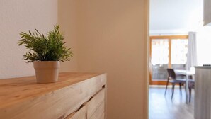 Un comptoir en bois agrémenté d’une plante en pot, un coin cuisine avec une table et des chaises, et une vue sur un balcon ou un espace extérieur.