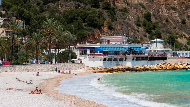 Een strand met een restaurant en een rotsachtige klif op de achtergrond.