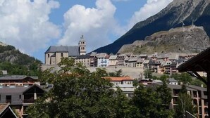 A town with a prominent church featuring a bell tower, surrounded by residential buildings and a mountain backdrop. - 200m from resort center, 3rd floor, balcony, tv, ski locker, 25m², Serre Chevalier (Briançon)