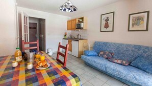 Un petit espace de vie chaleureux et accueillant, avec une table à manger dressée pour le petit-déjeuner, un canapé bleu et, au fond, une petite cuisine.