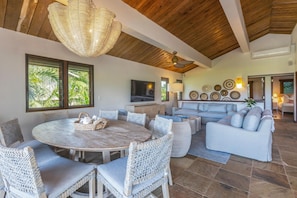 A spacious living area with a round dining table surrounded by wicker chairs, a sofa set, and a ceiling fan.