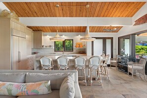 A modern kitchen with a wooden ceiling, a dining area with wicker chairs, and a view of greenery outside. - Nalu Hanalei, Stunning Home by the Beach TVR#5123 (Hanalei)