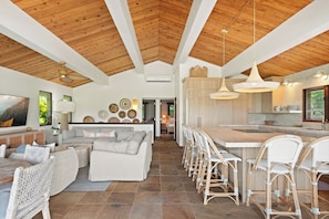 A spacious living area with a high ceiling, a dining area with wicker chairs, and a kitchen with a large island. - Nalu Hanalei, Stunning Home by the Beach TVR#5123 (Hanalei)