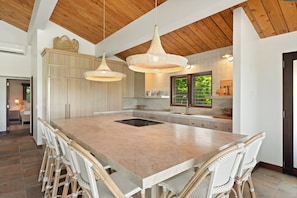 Une cuisine spacieuse avec un grand îlot central, un plafond en bois et des chaises en osier.