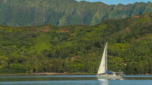 A sailboat on a calm lake with a forested mountain in the background.