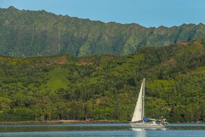 A sailboat on a calm lake with a forested mountain in the background.