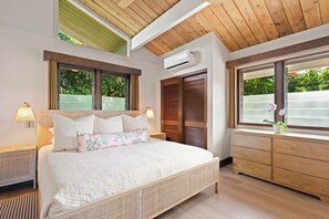 A bedroom with a bed, bedside lamps, a window with a view, a wooden ceiling, and an air conditioning unit. - Nalu Hanalei, Stunning Home by the Beach TVR#5123 (Hanalei)