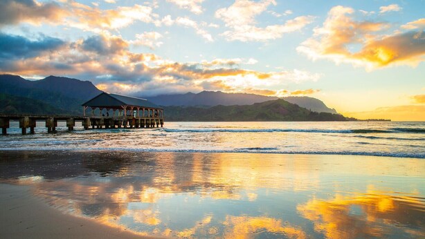 A pier extending into calm waters with a mountainous backdrop and a clear sky.