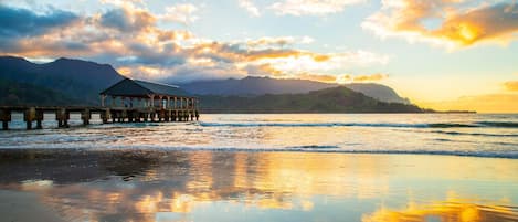 A pier extending into calm waters with a mountainous backdrop and a clear sky.
