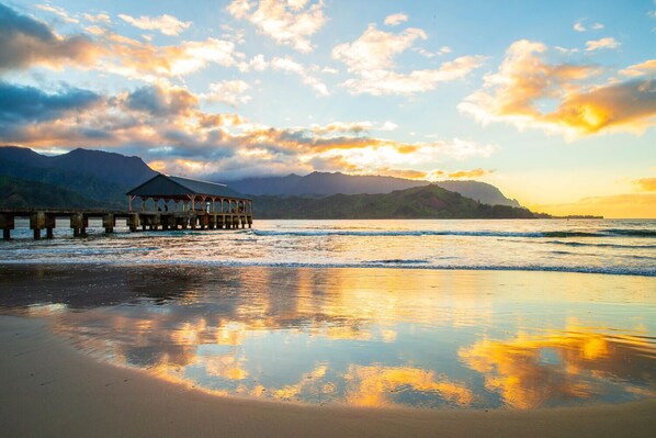 A pier extending into calm waters with a mountainous backdrop and a clear sky.