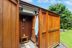 Un espace de douche extérieur en bois, avec une marche et une serviette accrochée à la porte.