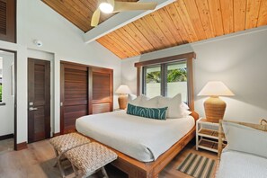 Un dormitorio con techo de madera, una cama grande con almohadas, dos lámparas de noche, una ventana con vistas y un banco.