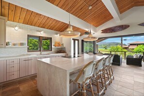 Una cocina moderna con una isla grande, techo de madera y amplios ventanales con vistas a un paisaje exuberante.