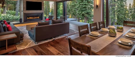 A modern living room with a fireplace, large windows, and a dining area.