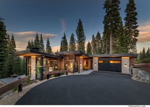 A modern house with a large driveway, surrounded by tall trees.