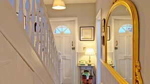 A staircase with white balusters, a wall-mounted telephone, and a large mirror reflecting a door with a window.