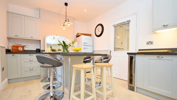A modern kitchen with white cabinets, a central island with stools, a vintage radio, and a clock on the wall.